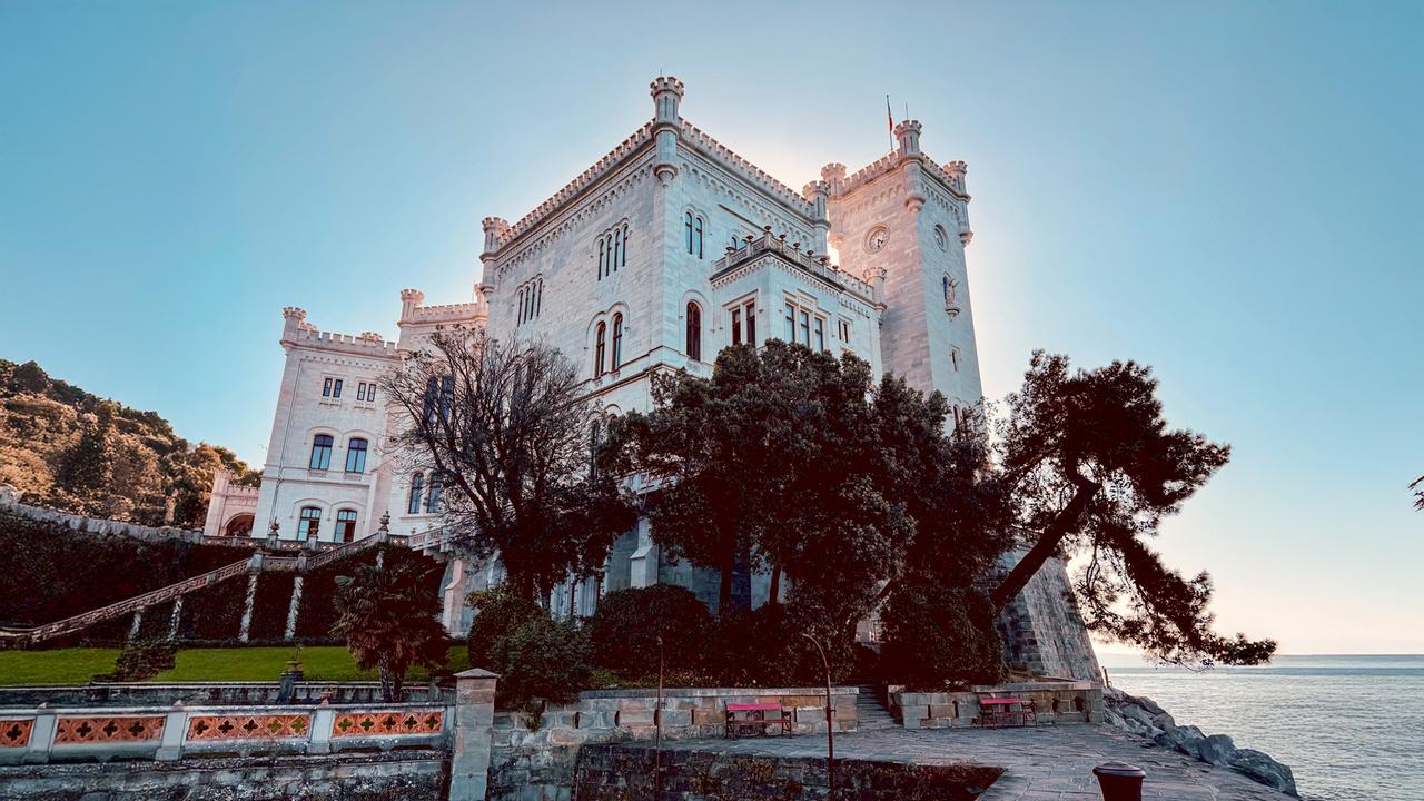 Das Schloss Miramare bei Triest mit seiner weißen Fassade, umgeben von Bäumen, mit Blick auf das Meer.