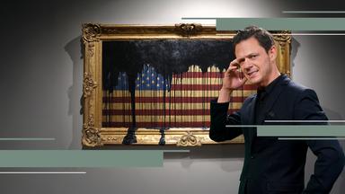 Jo Schück mit kritischem Blick vor amerikanischer Flagge in Bilderrahmen