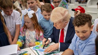 Ein älterer Mann im Anzug malt an einem Tisch, umringt von Kindern.