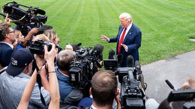 Ein älterer Mann im Anzug steht gestikulierend vor einer Schaar Reporter mit Kameras und Mikros.