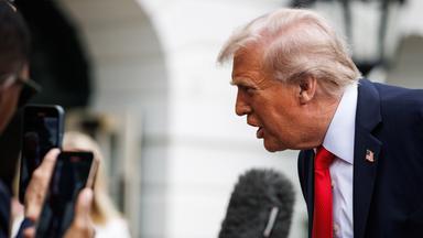 Ein älterer Mann im Anzug beugt sich vor und spricht in Handy-Kameras und Mikros, die ihm entgegen gehalten werden.