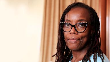 Porträtbild einer schwarzen Frau mit Rastalocken und großer Brille.