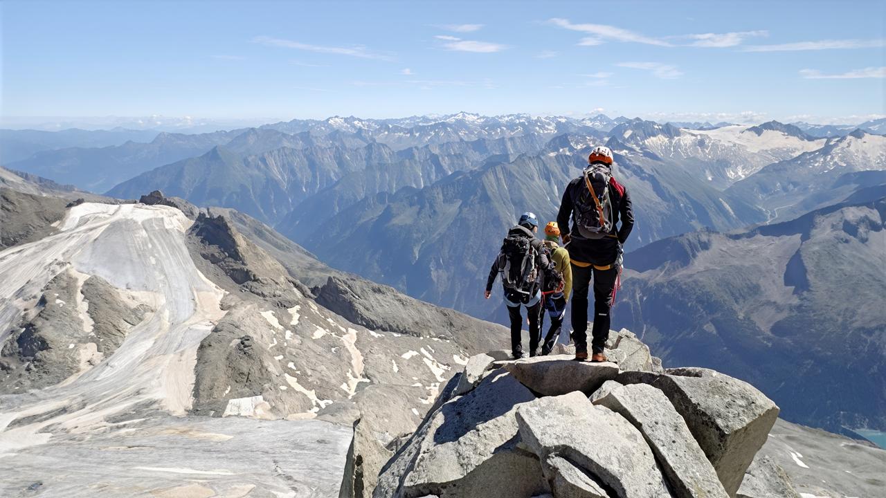 Seilschaft aus vier Bergsteigerinnen und Bergsteigern auf dem Grat des Olperers mit Blick über umliegende Gletscher und Gipfel bei klarer Sicht.