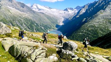 Eine Gruppe von Menschen wandert vor alpiner Kulisse mit Stausee
