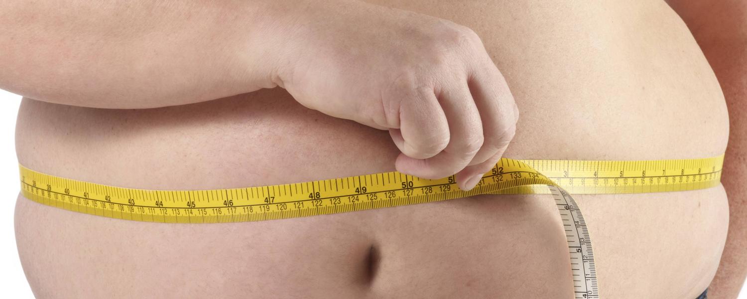 Ein übergewichtiger Mann misst mit einen Maßband seinen Bauchumfang