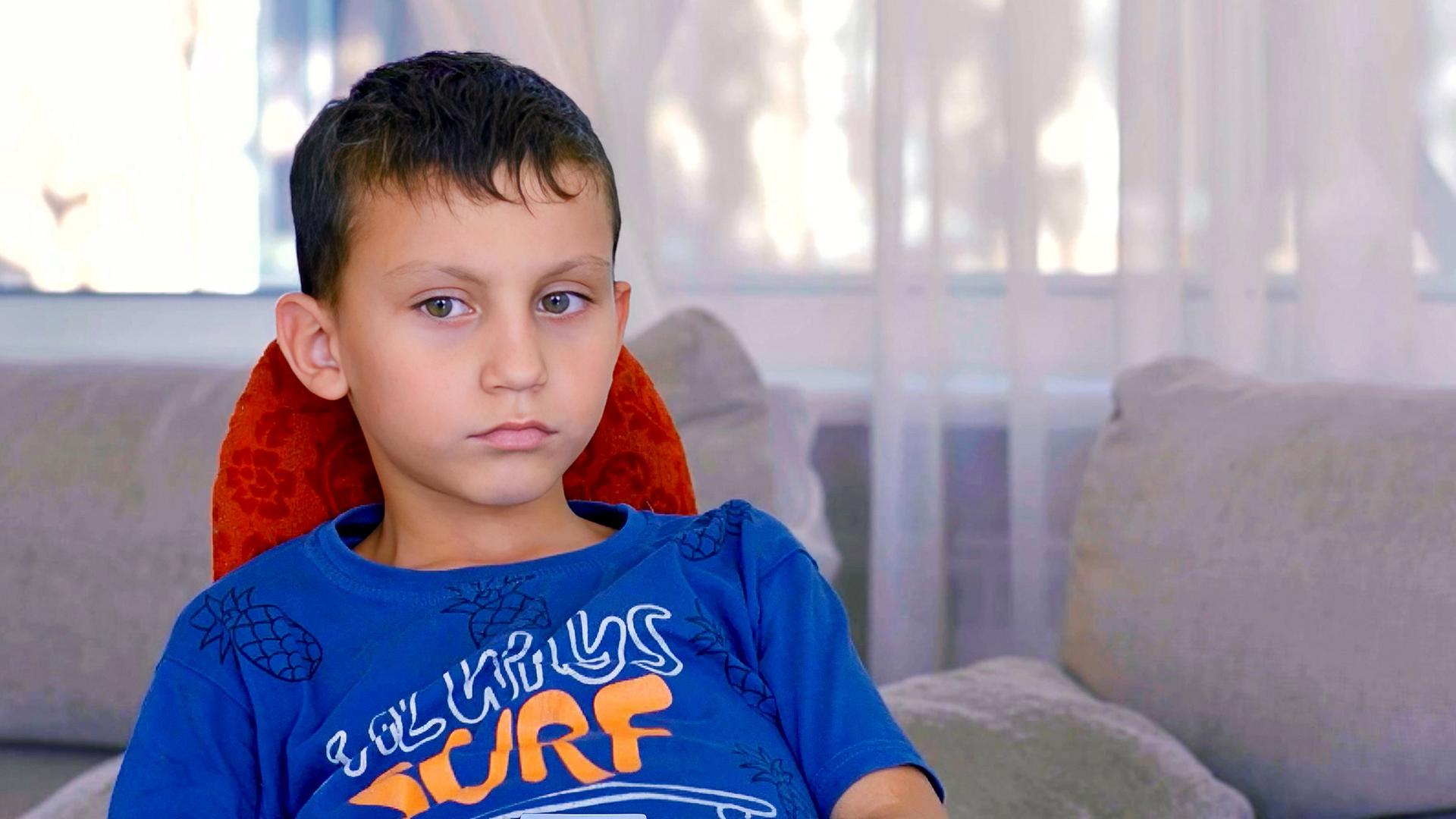 Ein kleiner Junge auf einem Stuhl sieht mit betroffenem Blick zur Seite.