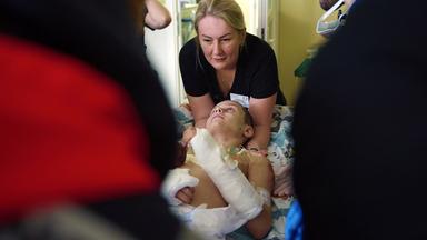 Ein Junge mit verbundenem Rumpf und Armen wird von Helfern auf eine Trage gebettet.