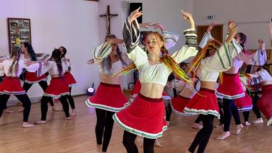 Jugendliche in roten Röcken und kurzen weißen Blusen tanzen in einem Raum.