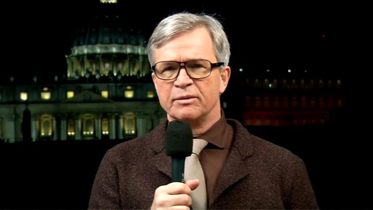 Mann mit grauen Haaren, Brille und Mikrofon.