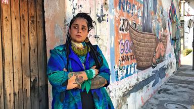 Die Hip-Hop Sängerin Audry Funk lehnt in einem Blauen Blazer an einer bunt angemalten Hauswand