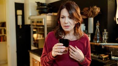 Eine Frau hält mit besorgtem Blick ein Glas in der Hand.