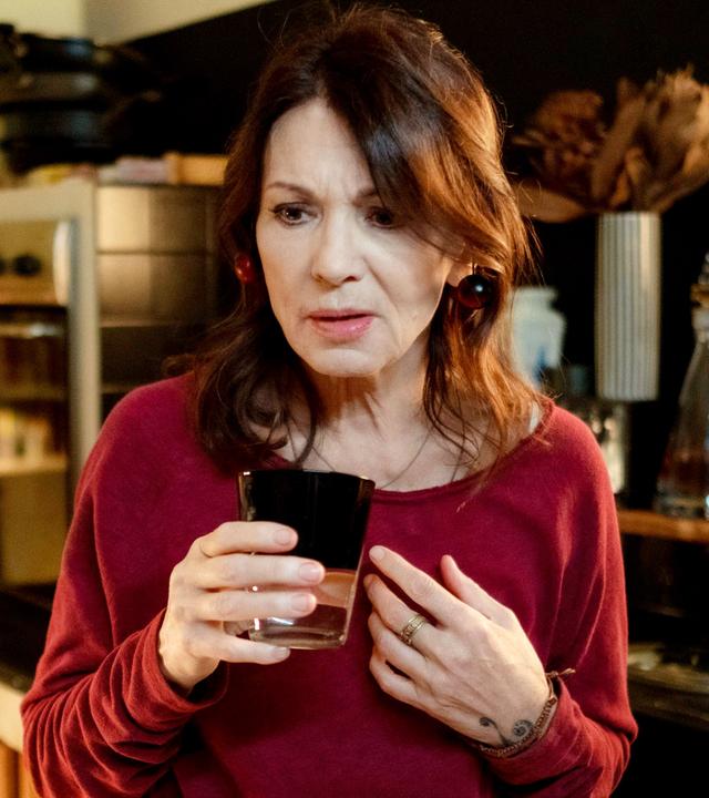 Eine Frau hält mit besorgtem Blick ein Glas in der Hand.