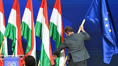 Mann stellt Europa-Flagge zu einer Reihe von ungarische Flaggen hinter einem Redner-Pult.