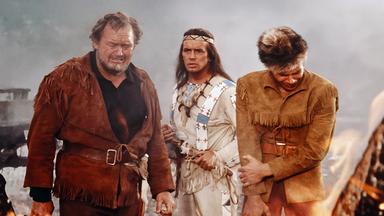 Baumann (Walter Barnes), Winnetou (Pierre Brice) und Martin Baumann Jr. (Götz George) stehen betroffen zwischen den brennenden Trümmern der Farm.