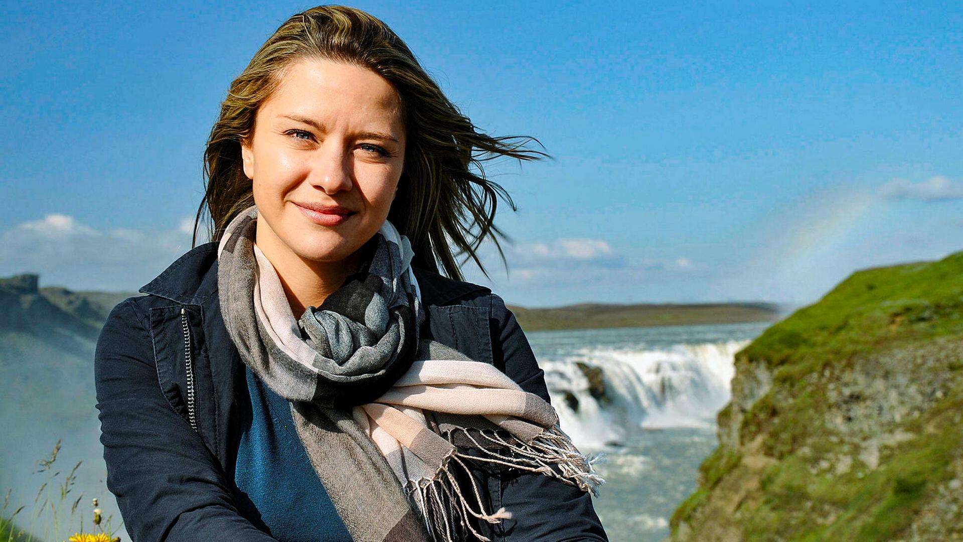 Eine junge Frau mit wehendem Haar vor einem Wasserfall