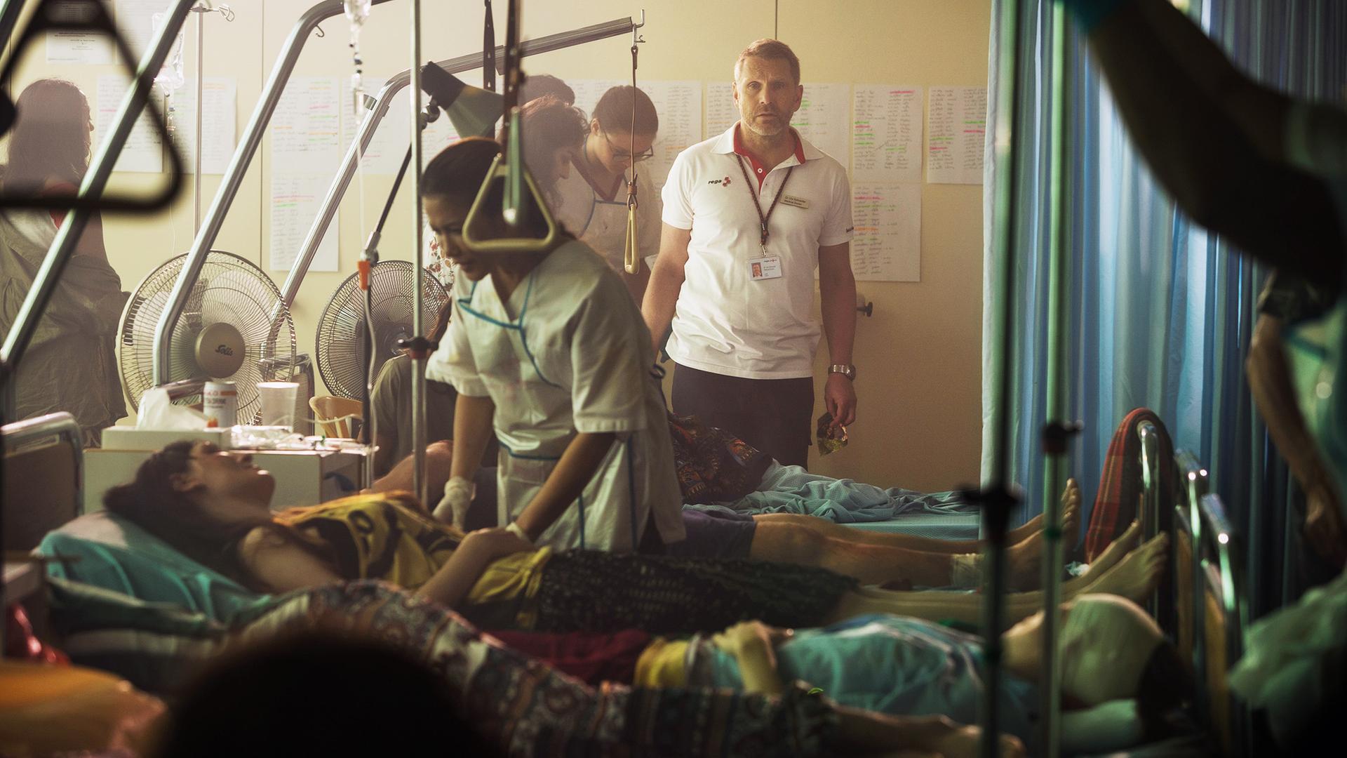 Ein Schauspieler stellt einen Arzt dar, der in einem thailändischen Krankenhaus nach einer vermissten Person sucht. Die Szene erinnert an die humanitäre Katastrophe des Tsunamis von 2004.