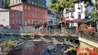Ansicht einer Altstadt mit einem kleinen Flüsschen. Der Moderator und die Autorin stehen auf einer Brücke darüber.
