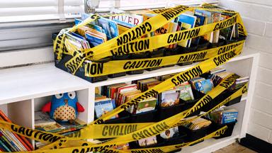 Mit gelbem Klebeband Caution beklebte Kinderbücher in einem Regal am Fenster
