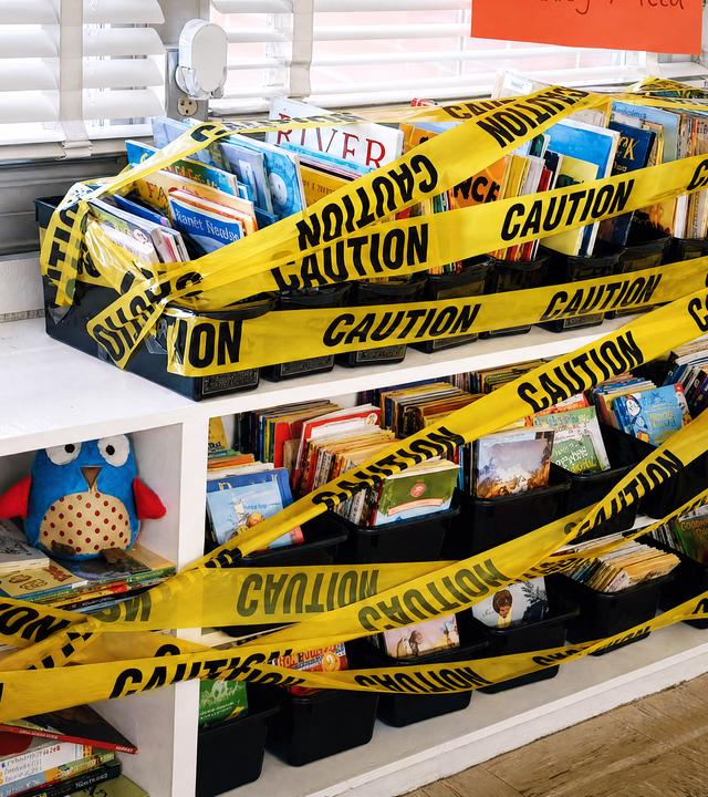 Mit gelbem Klebeband Caution beklebte Kinderbücher in einem Regal am Fenster