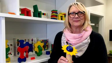 Eine blonde Frau steht vor einem Regal voller Holzspielzeug
