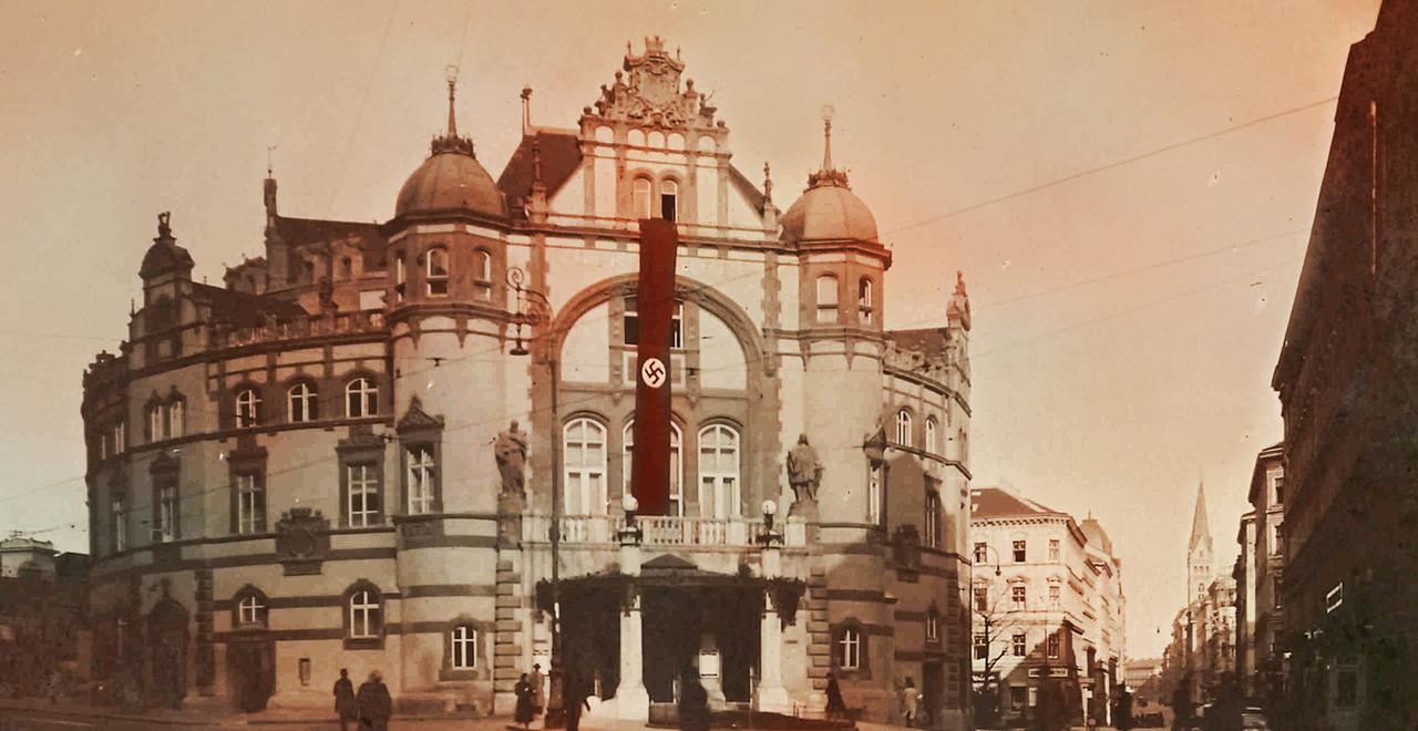 Ein braun-rötlich eingefärbtes schwarz-weiss Foto eines alten Gebäudes mit Hakenkreuzfahne an der Fassade 