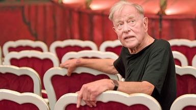 Claus Peymann sitzt im Zuschauerraum in einem Theater