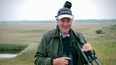 Ein Mann mit Kamera, Stativ und Fernglas über der Schulter