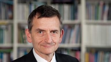 Mann in Anzug mit roter Krawatte vor einem Bücherregal