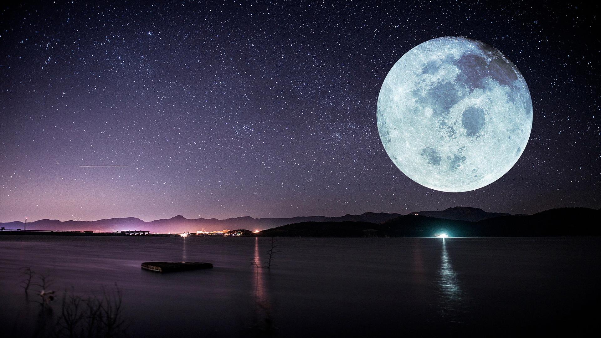 Eine Meeresküste bei einer Vollmondnacht. Der Himmel ist voller Sterne, im Hintergrund sieht man Berge. Der Mond ist riesig und sehr deutlich zu sehen.