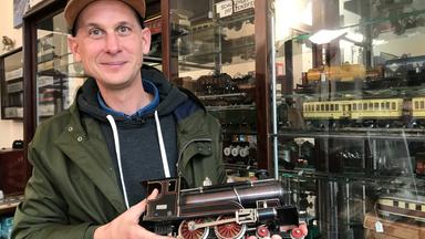 Ein Mann hält stolz einen Waggon einer Modelleisenbahn in der Hand.