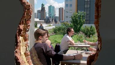 Menschen sitzen in Rotterdam auf einer Dachterrasse. Im Hintergrund die Hochhäuser der Stadt.