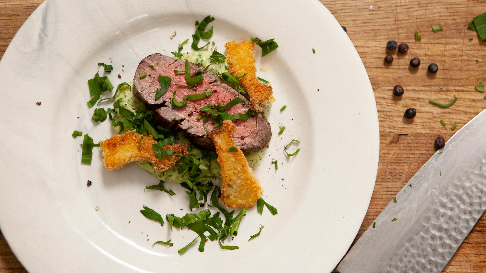 Mariniertes Rinderfilet mit Pastikanen-Kartoffel-Püree an gebratenen Kräuterseitlingen auf einem Teller.