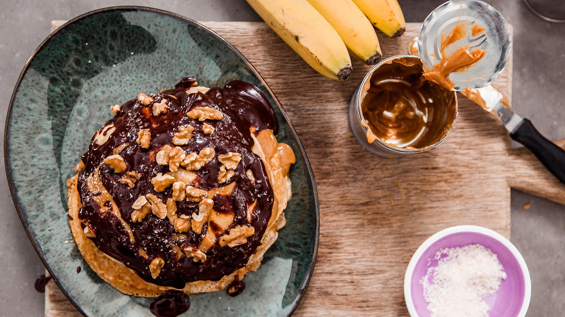 Pfannkuchen mit schokosoße und Walnüssen auf einem Teller.