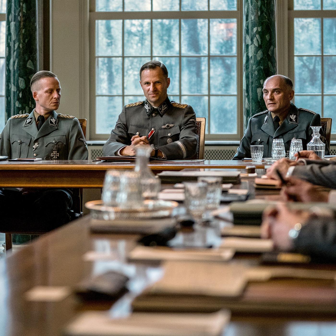 Im Besprechungssaal sitzen die Teilnehmer in Uniformen an einem Konferenztisch. 