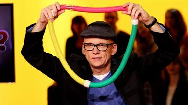 Ein Mann hält sich eine bunte, breite Kette vor den Kopf.