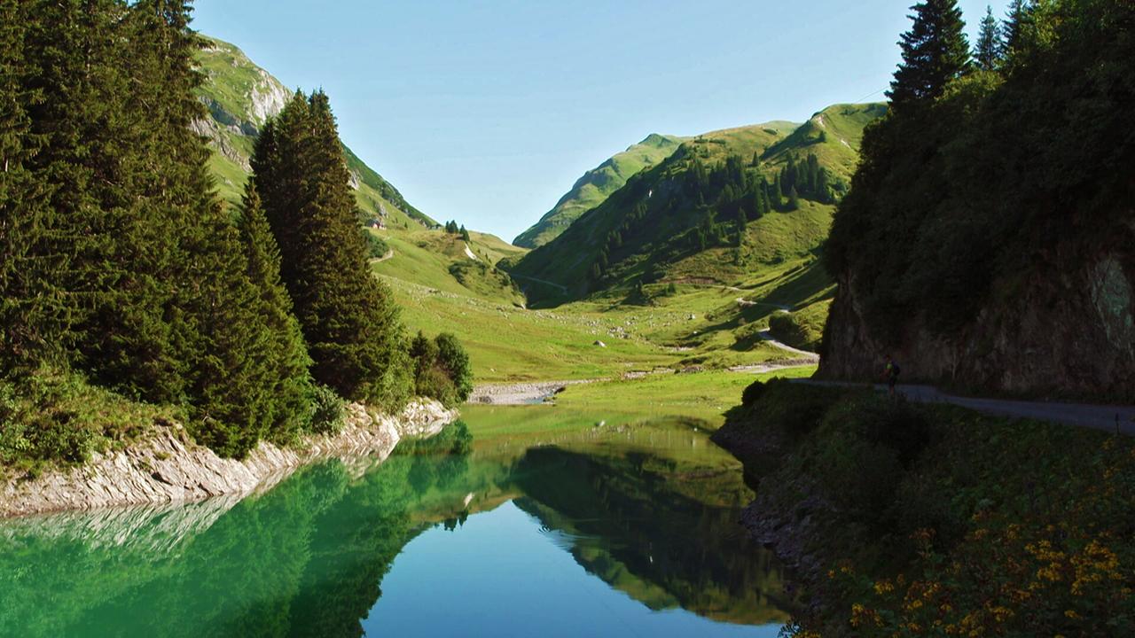 Ein Bergsee zwischen grünen Wiesen und blauem Himmel