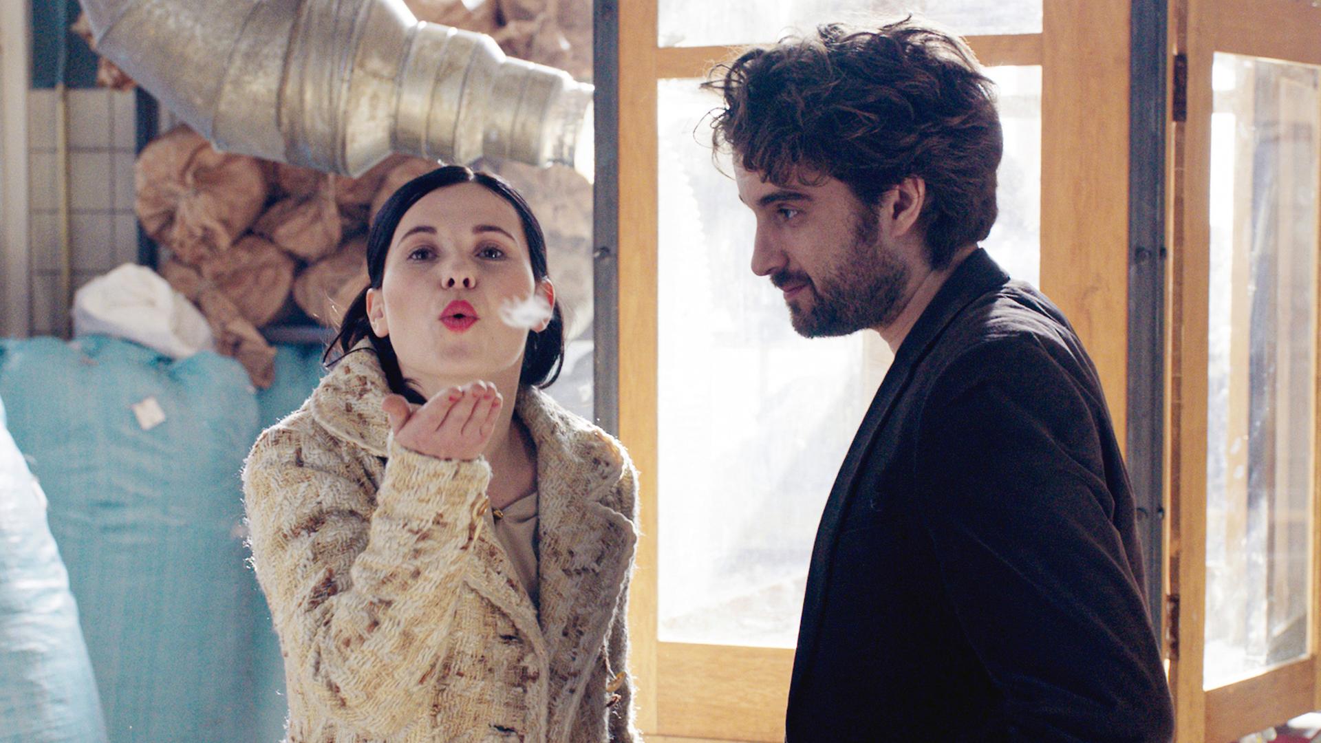 Eine Frau pustet eine Feder in die Luft, ein Mann schaut ihr zu