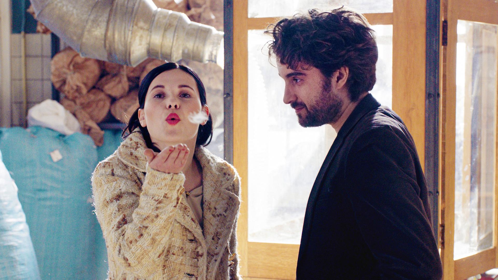 Eine Frau pustet eine Feder in die Luft, ein Mann schaut ihr zu