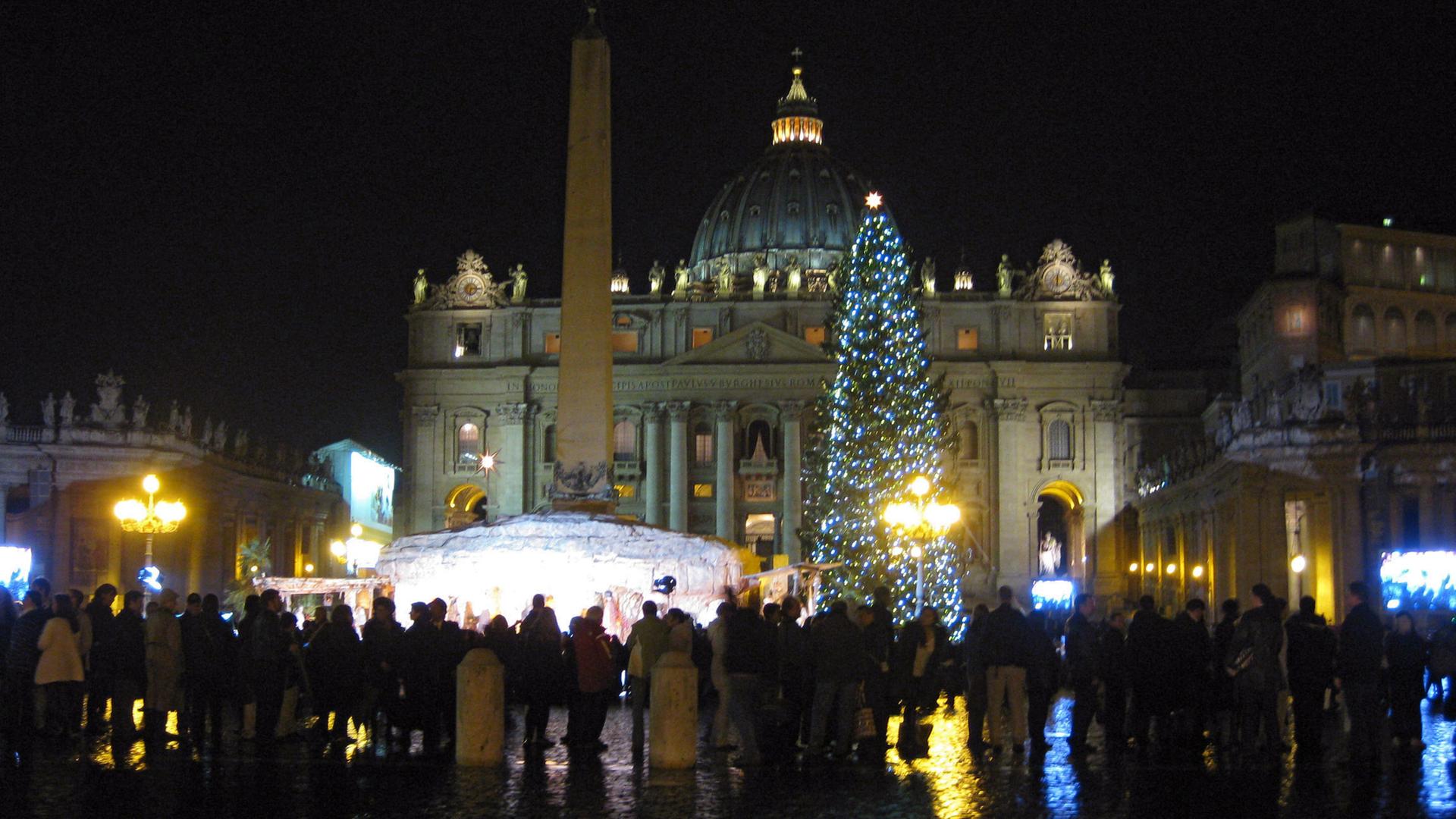 Blick auf den weihnachtlich geschmückten Petersplatz mit festlich leuchtendem Weihnachtsbaum und Besuchern am Abend.
