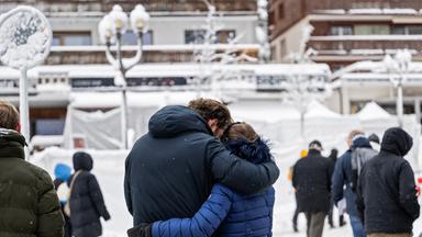 Trauernde Menschen stehen vor der mit Schnee und weissen Folien bedeckte Bar, wo das für viele tödliche Feuer ausgebrochen war