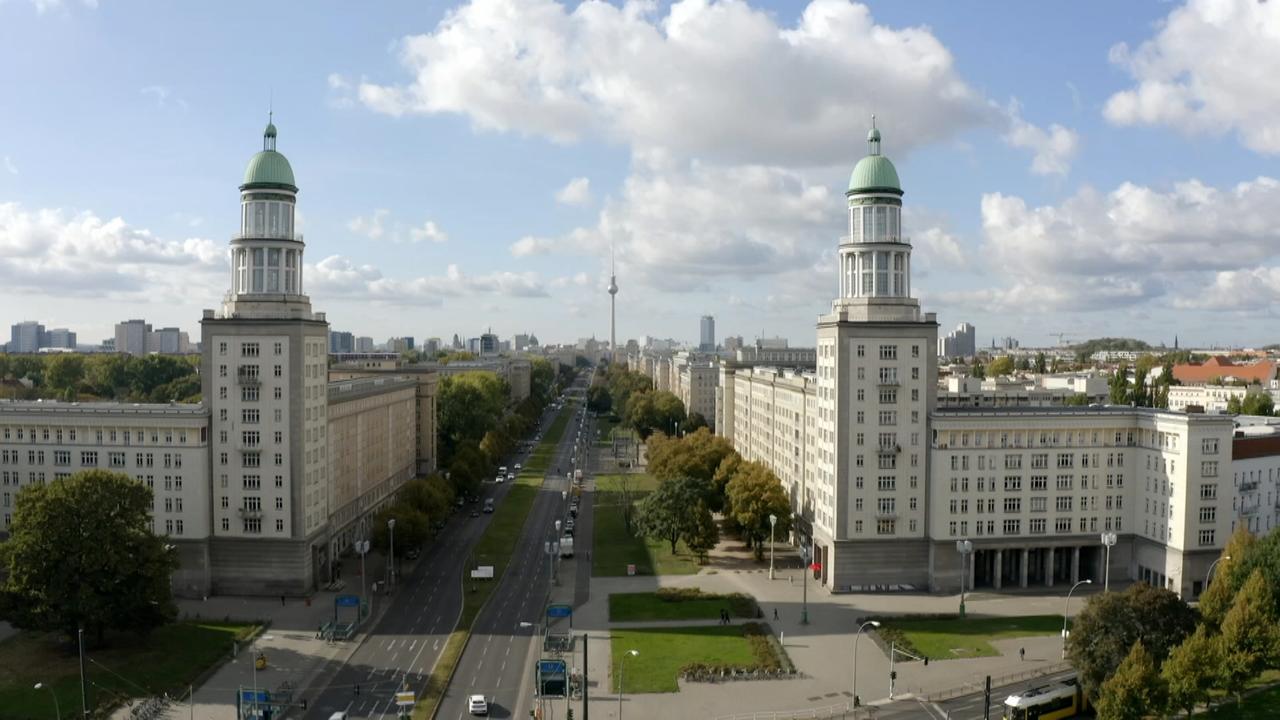 Blick auf die Karl-Marx-Allee in Berlin mit Türmen zu beiden Seiten und im Hintergrund der Fernsehturm