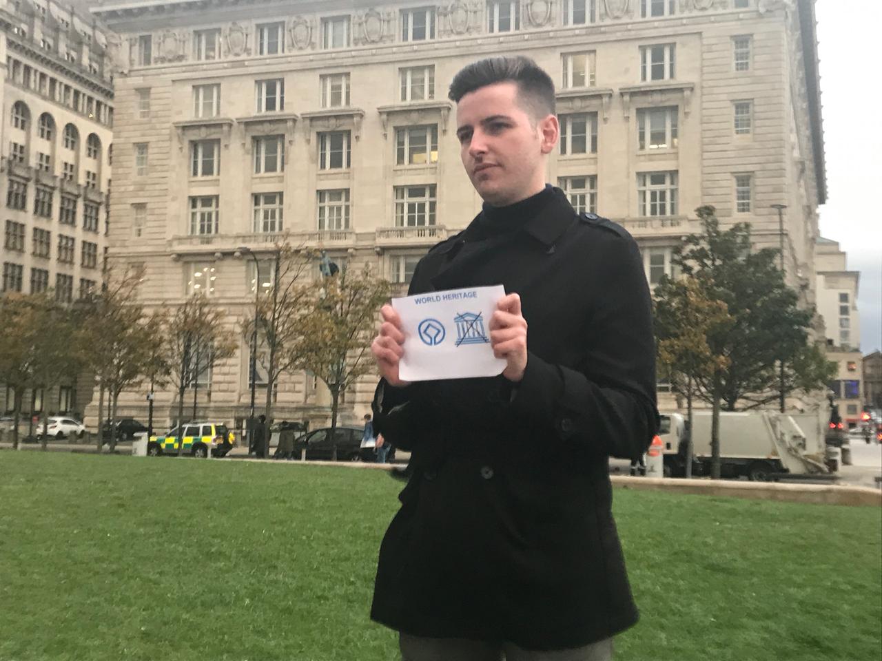 Junger Mann hält durchgestrichenes Unesco-Label in der Hand