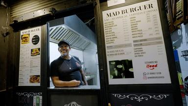 Ein Mann schaut lachend nach vorn in einer Imbissbude mit Namen Mad Burger.