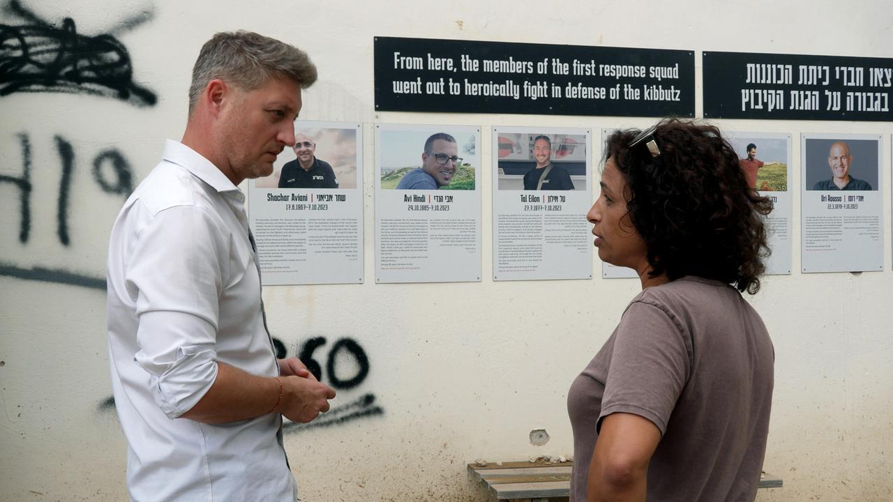 Ein Mann und eine Frau vor einer Wand mit mehreren Portraits und Text dazu.