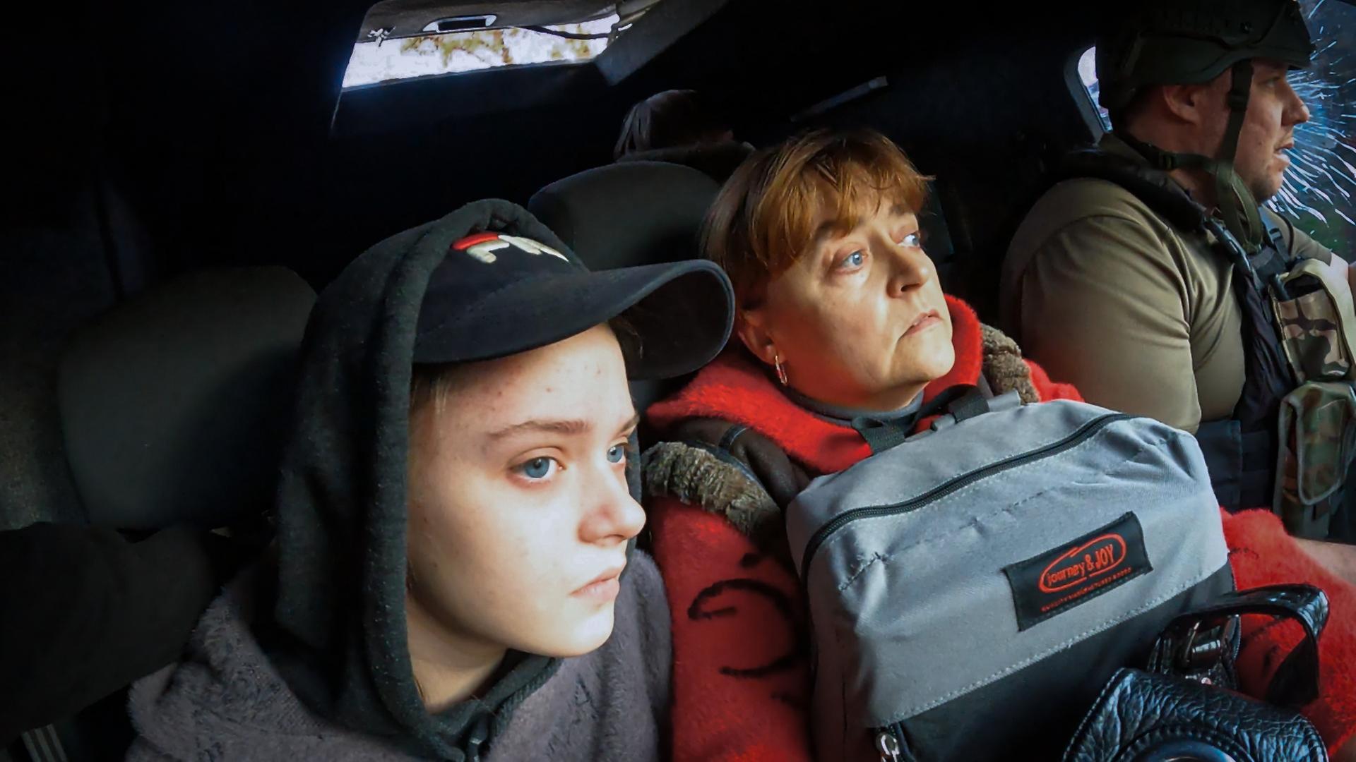 Mutter Natalya sitzt mit Rucksack auf dem Schoß, neben ihrer Tochter Eleni und einem Fahrer im Auto des Evakuierungsteams.