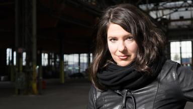 Das Portrait einer jungen Frau mit braunen Haaren, schwarzem Schal und Lederjacke.