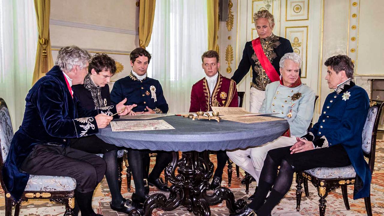 Mäner in historischen Uniformen um einen Tisch sitzend.