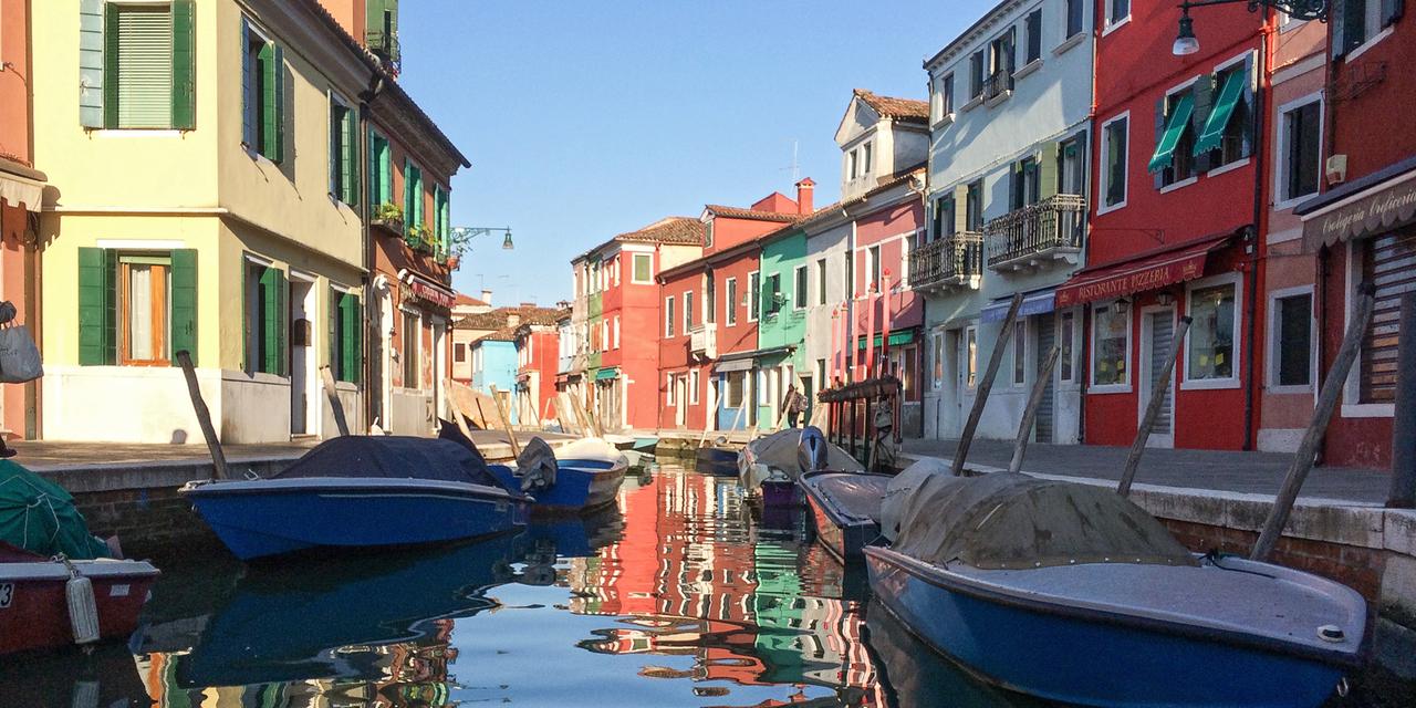 Ein Kanal in Venedig umgeben von Häusern mit kleinen Booten darauf.