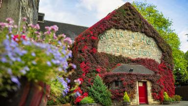 Ein bewachsenes Gebäude derBlair Athol Destillerie – Whiskybrennerei in Pitlochry, Schottland. Blumen im unscharfen Vordergrund.