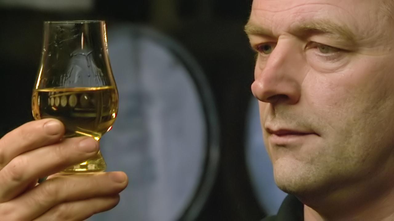 Ein Mann begutachtet ein Glas mit Whisky, das er in seiner Hand hält.